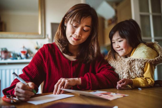 jovem mãe bonita escrevendo cartão para família com sua linda filha em casa