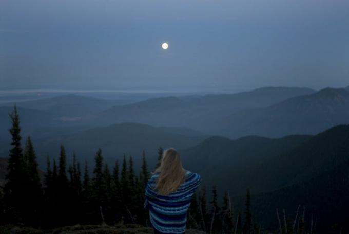 mulher enrolada em cobertor olhando a paisagem montanhosa com lua cheia, retrovisor