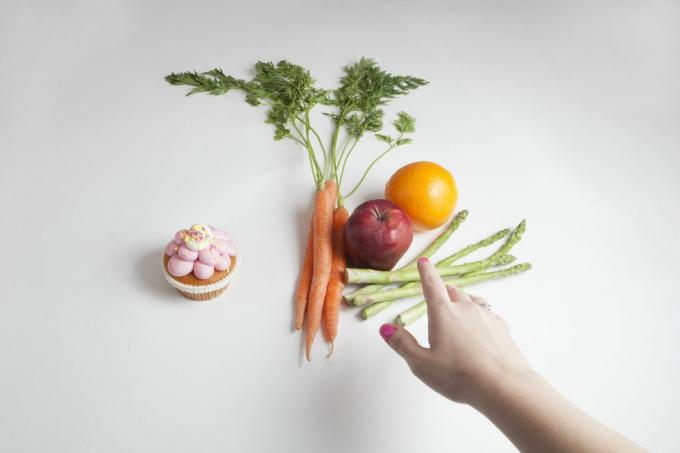 uma mão pega uma variedade de frutas e legumes em vez de um cupcake