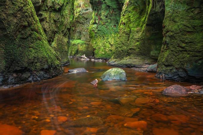 Rio vermelho sangue em um desfiladeiro verde. Devil's Pulpit, Finnich Glen, perto de Killearn, Escócia, Reino Unido