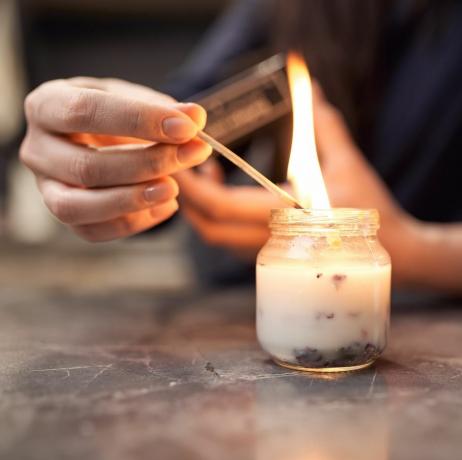 cortar mulher anônima com fósforo aceso acendendo vela aromática em jarra de vidro colocada na mesa de mármore em casa