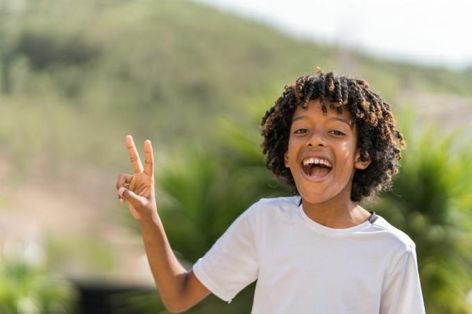 Menino afro-americano de 10 anos rindo alto enquanto fazia o sinal de paz