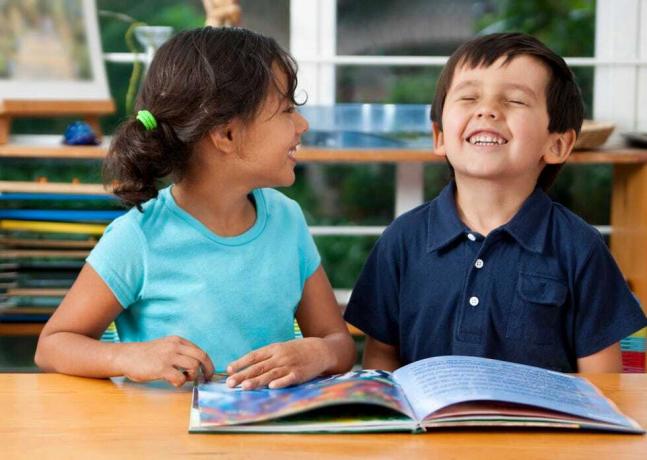 duas crianças rindo e desfrutando de um livro na escola