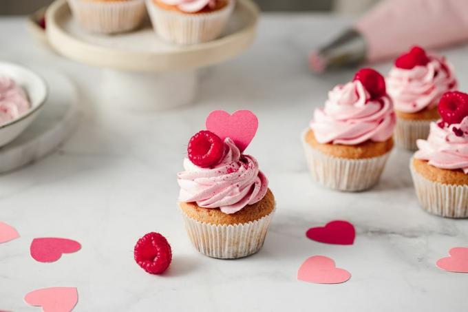 cupcakes de framboesa recém-feitos no balcão da cozinha deliciosos cupcakes cor de rosa com framboesa e cobertura de coração de papel