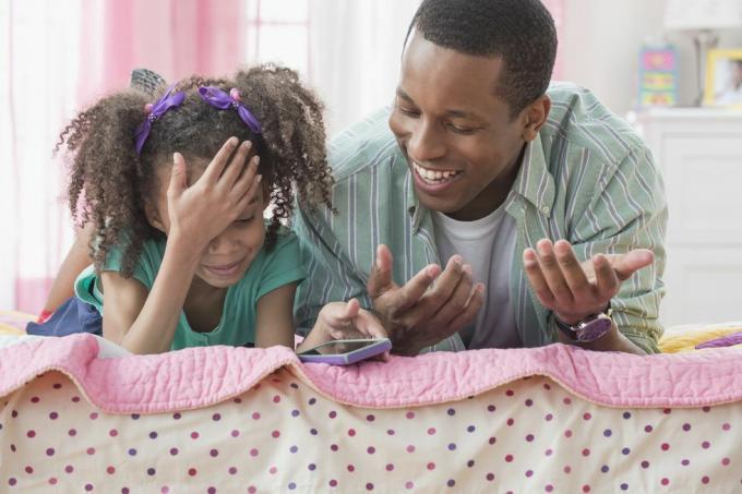 pai e filha usando celular juntos na cama