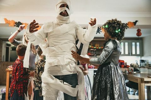 grupo de crianças vestindo um dos pais no papel higiênico para parecer uma múmia durante uma festa de halloween