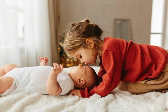 adorável criança beijando irmãzinha deitada na cama branca