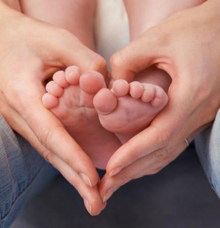 Pés da criança segurados pelas mãos do adulto em forma de coração