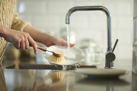 uma mulher usa uma escova sem plástico para limpar a louça na pia da cozinha, feche