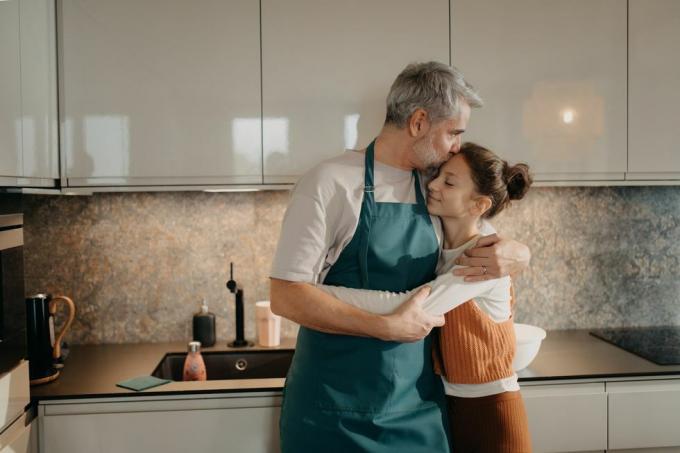 homem maduro com sua filha adolescente abraçada na cozinha