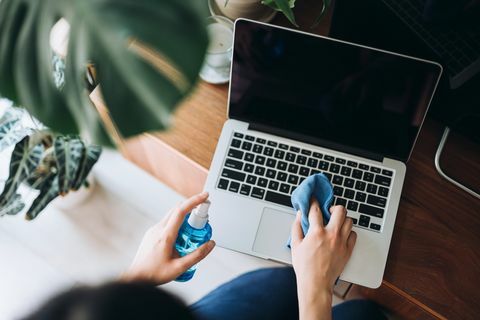 foto recortada de uma jovem limpando a superfície do laptop com spray de limpeza e pano antiestático em casa