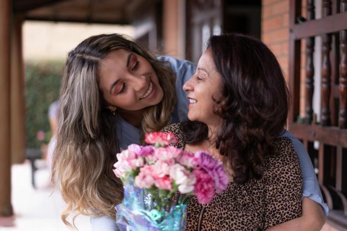 filha amorosa abraçando a mãe por trás surpreendendo-a com flores para os conceitos de comemoração do dia das mães