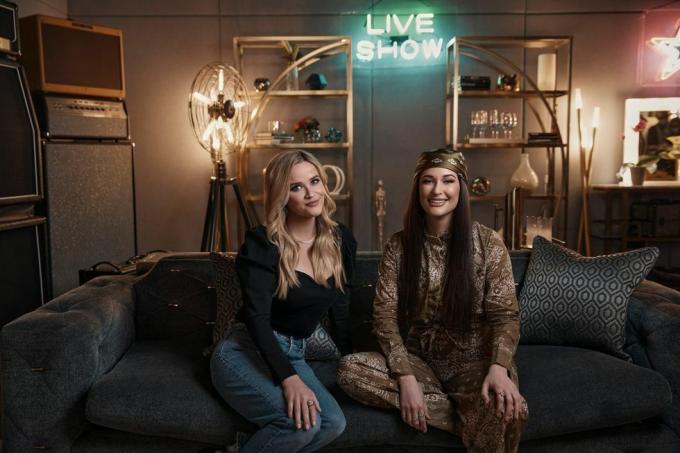 reese witherspoon e kacey musgraves sentados lado a lado no sofá