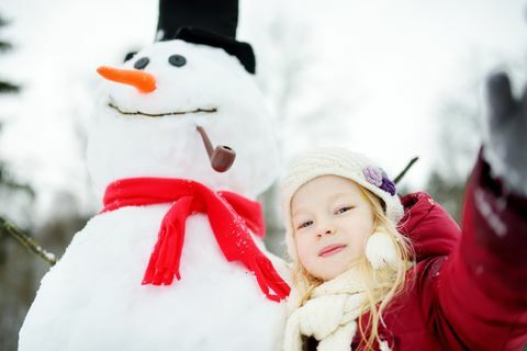 Adorável menina construindo um boneco de neve no belo parque de inverno. Bonita criança brincando na neve.