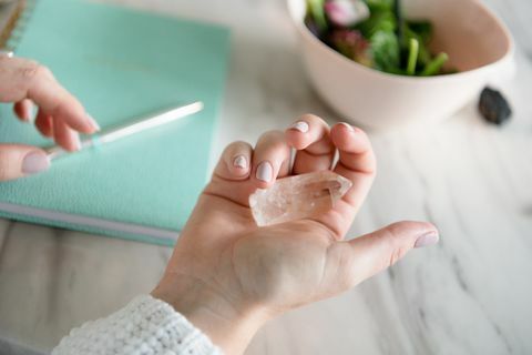 mão de mulher segurando cristais de cura com notebook em segundo plano