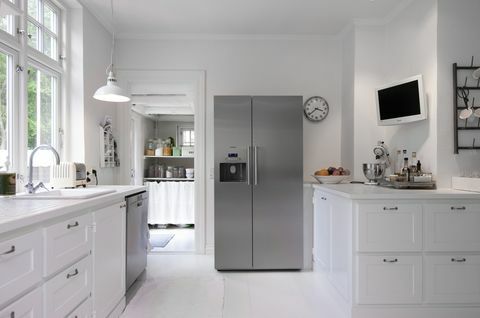 Cozinha branca com geladeira vertical prata na renovação da casa de Hanne Davidsen, Silkesborg, Dinamarca.