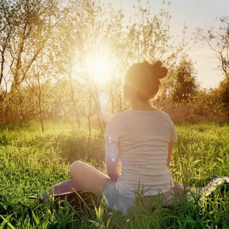 jovem sentada em posição de ioga apreciando o pôr do sol na natureza