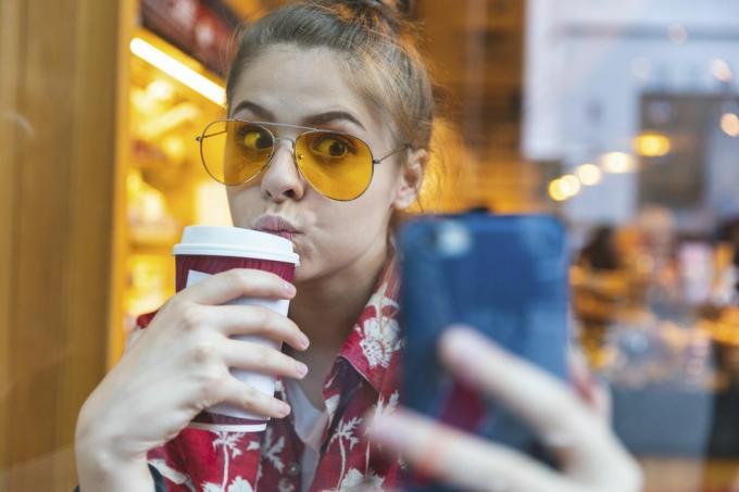 jovem do lado de fora em óculos de sol tirando uma selfie enquanto bebe um café para viagem