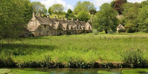 Vista de Bibury, Gloucestershire com prado de água em primeiro plano e casas de campo de ondulação de cotswold atrás