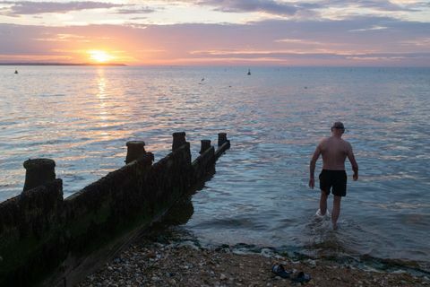 enquanto o sol se põe sobre a luz do dia e as águas calmas do estuário do Tâmisa, um nadador selvagem do mar entra na água para sua mergulho noturno regular, em 18 de julho de 2020, em whitstable, kent, inglaterra foto de richard baker em fotos via imagens getty