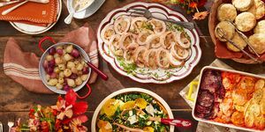 uma mesa posta com pratos de comida, incluindo rocambole de peru, salada de inverno, biscoitos, raízes gratinadas e cebolas agridoces