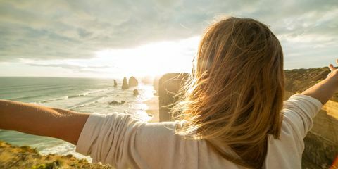 braços de mulher jovem estendidos ao pôr do sol