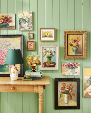 coleção de pinturas florais vintage exibidas em uma parede de beadboard verde