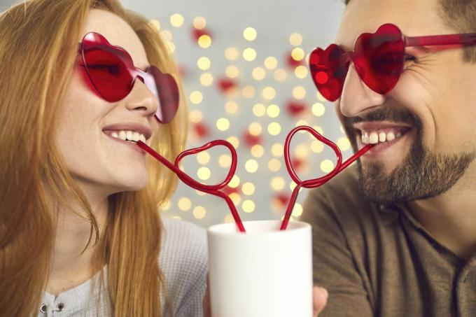 close-up retrato feliz jovem e mulher apaixonada em óculos de sol cor de rosa bebendo bebida de um copo através de canudos em forma de coração, aproveitando o momento engraçado do casal em um encontro divertido no dia dos namorados