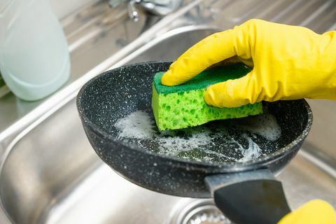 mão com uma esponja lava uma frigideira suja em água corrente