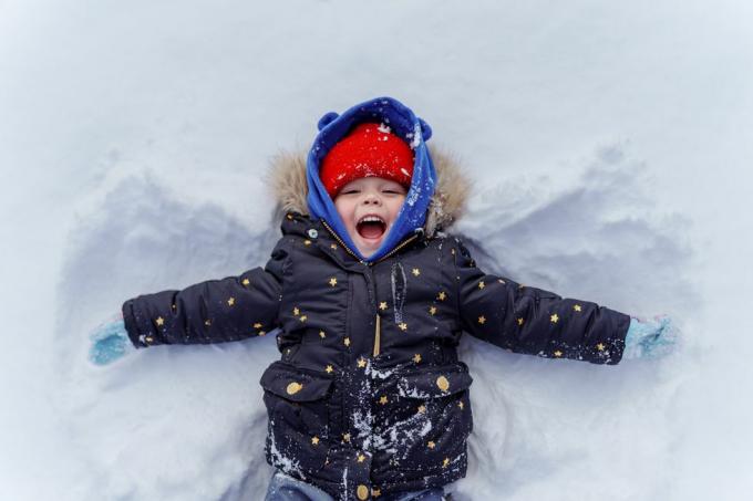 criança na neve fazendo anjo de neve