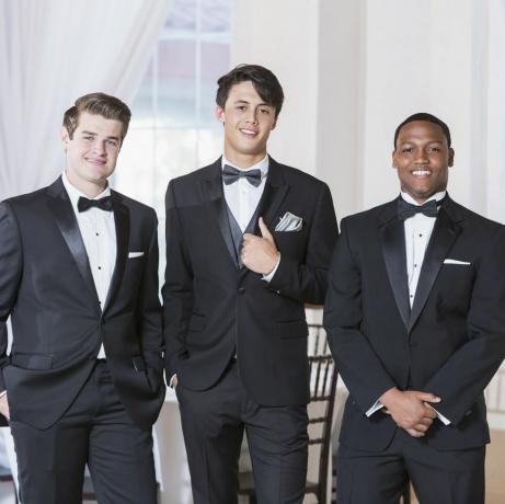 um grupo de três jovens multiétnicos vestindo smoking, parados em uma fila, sorrindo para a câmera, eles estão em uma festa, baile, casamento ou algum outro evento formal especial