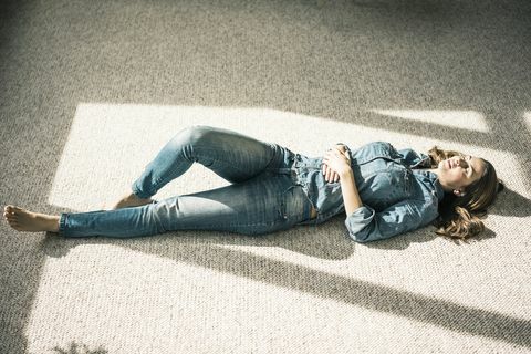 Jovem mulher deitada no tapete na sala de estar desfrutando da luz solar